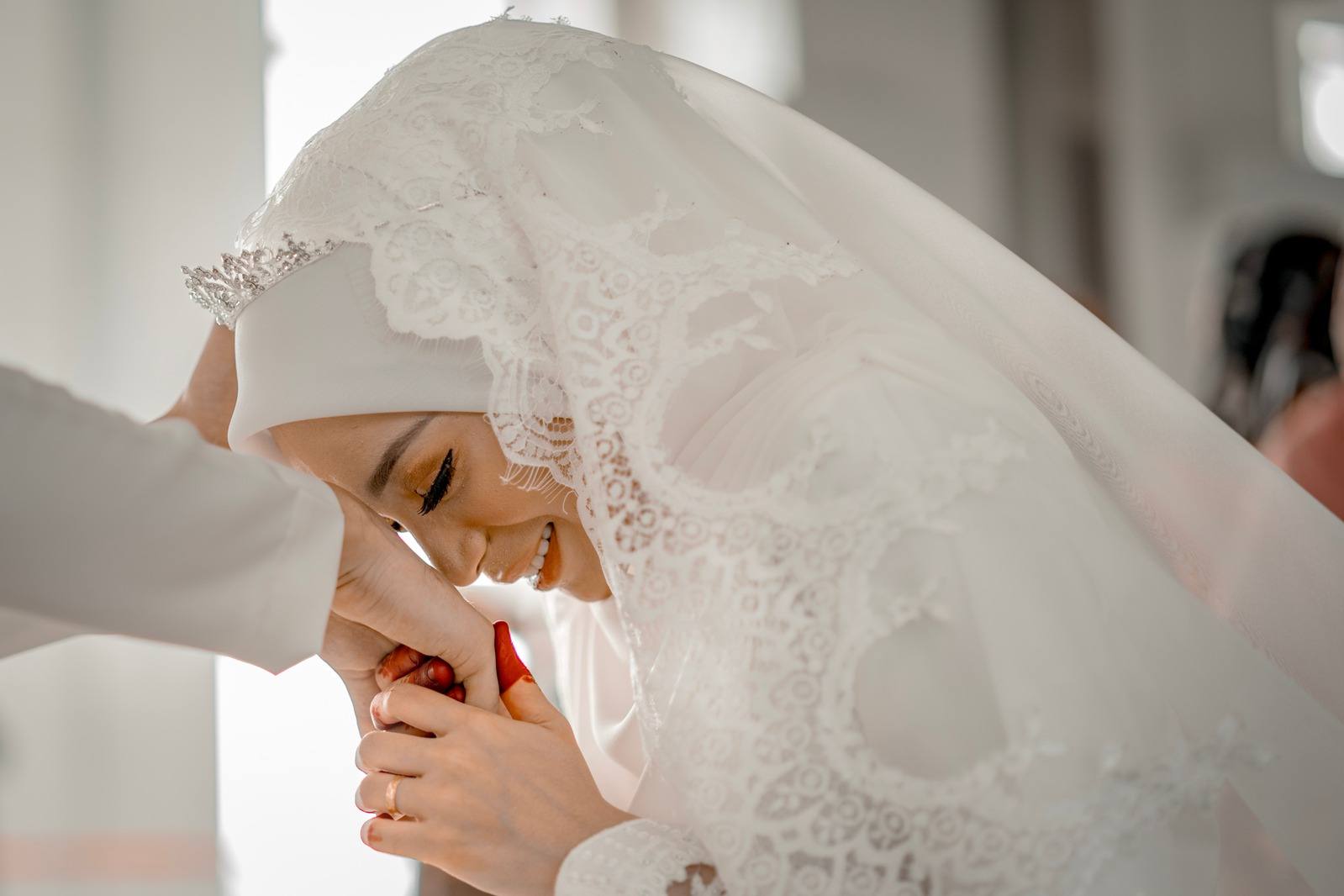 A bride in white kissing her husband's hand after their nikah