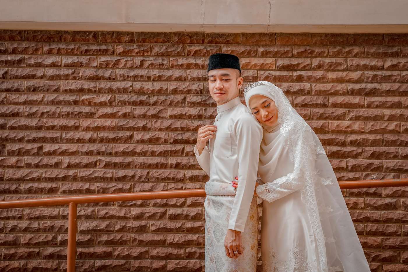 Iqbal and Ariana embracing in front of a terracotta brick wall
